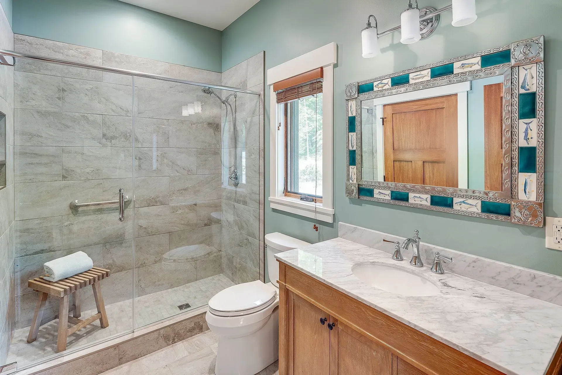 Bathroom with a glass shower, toilet, wooden vanity with marble countertop, and a decorative mirror.