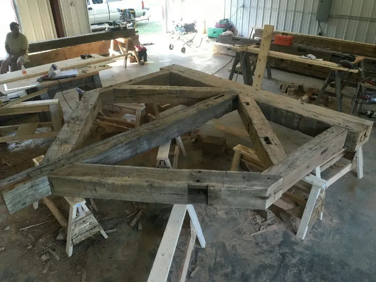 Wooden structure in a workshop, supported by sawhorses. Beams show aged wood and joinery.