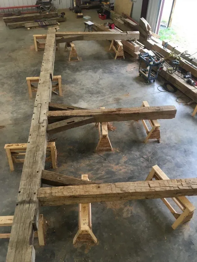 Wooden beams on sawhorses in a workshop, likely for restoration or construction.