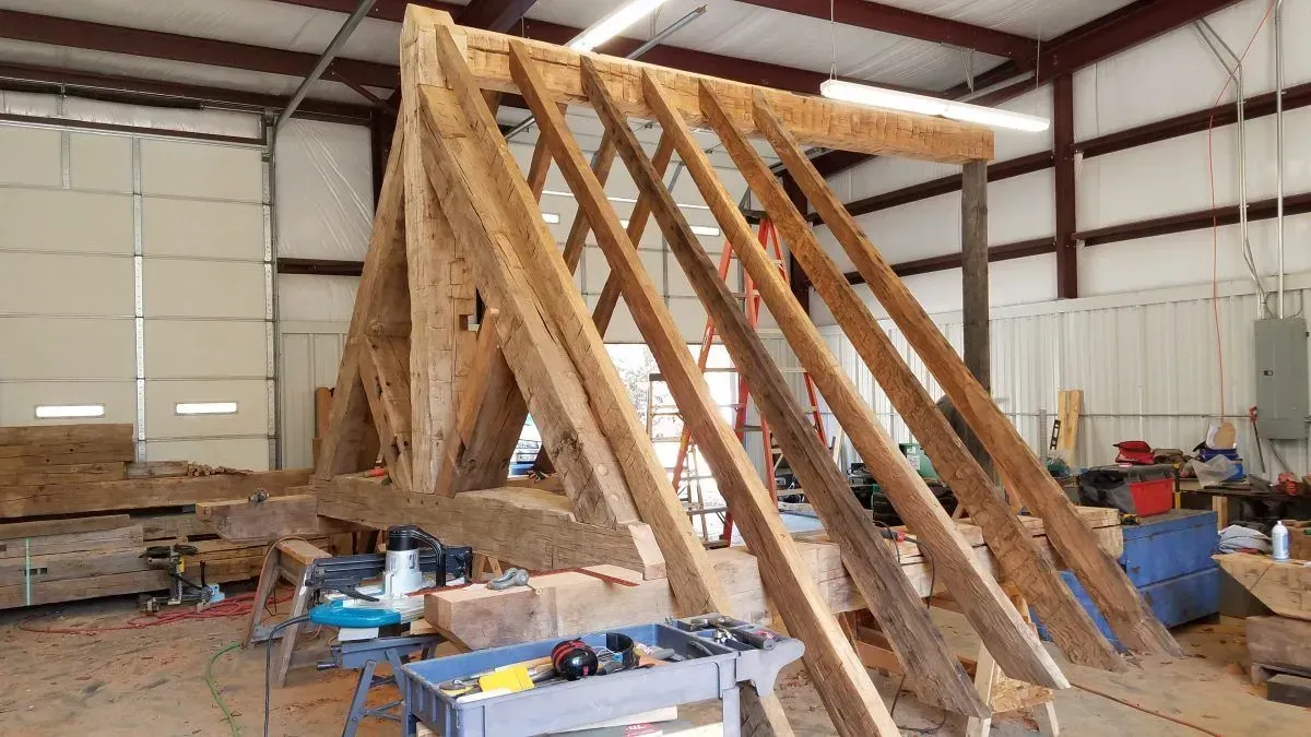 Wooden timber frame construction inside a workshop; rafters and supporting beams are visible.