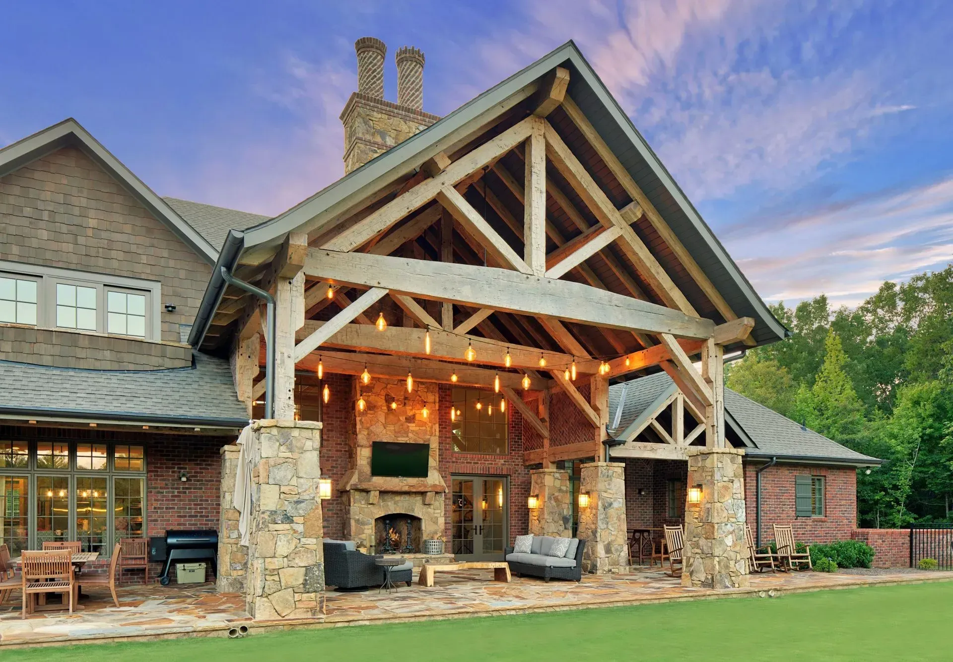 Outdoor covered patio with stone columns, fireplace, and string lights, attached to a brick home.