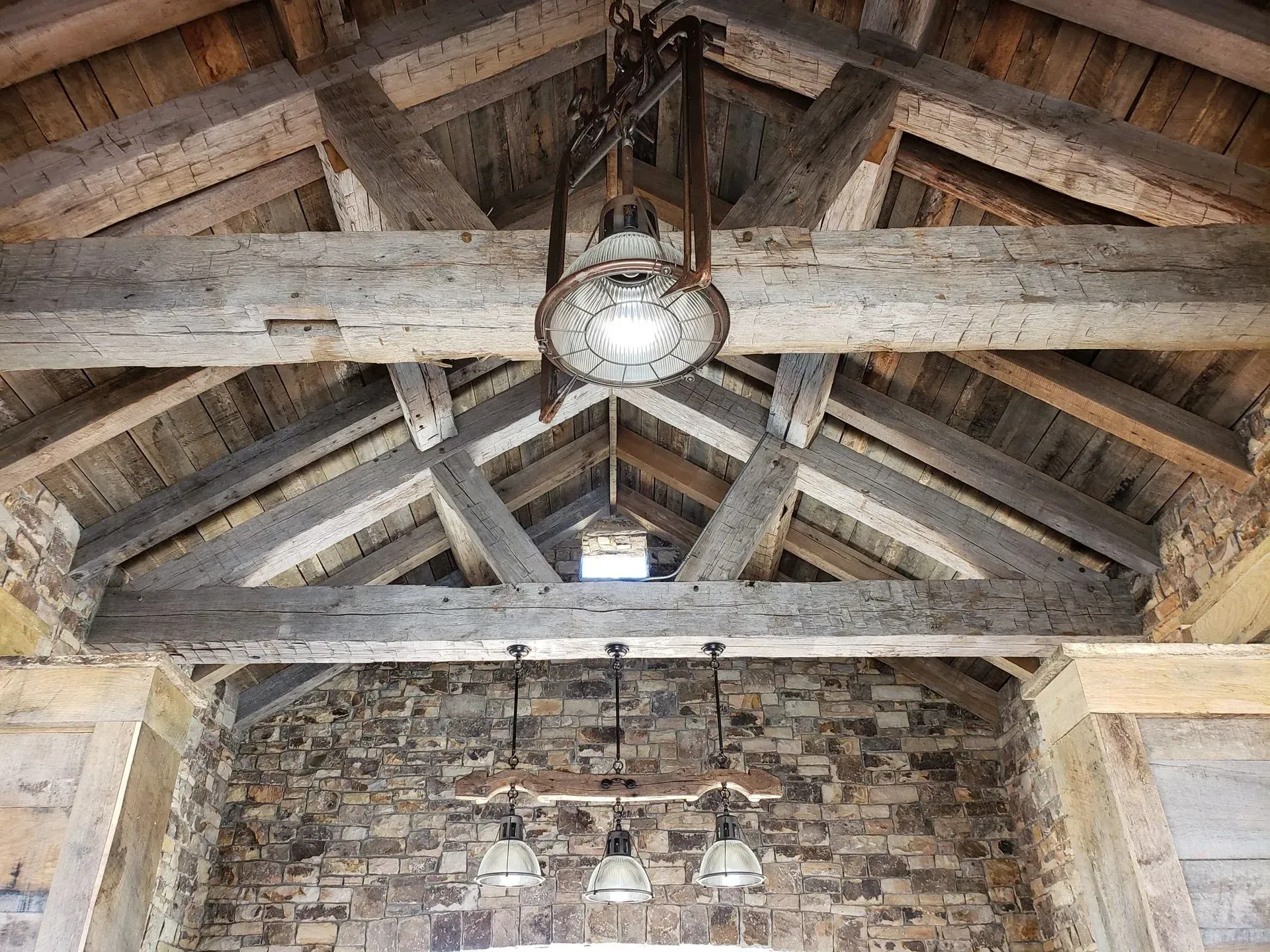 Wooden beam ceiling with hanging lights, stone wall.