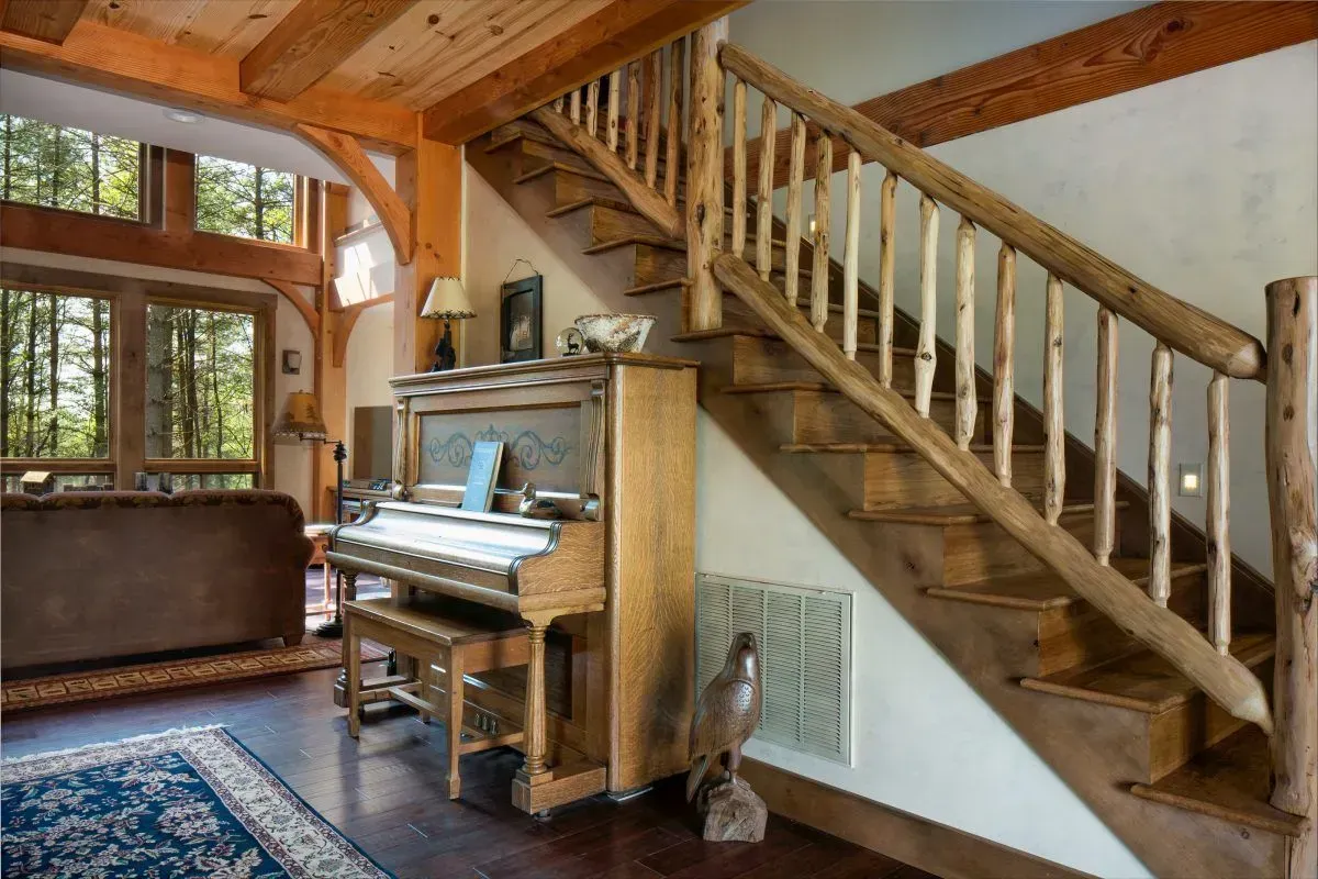 Wooden staircase and piano in a rustic, light-filled interior, with a view of trees outside.