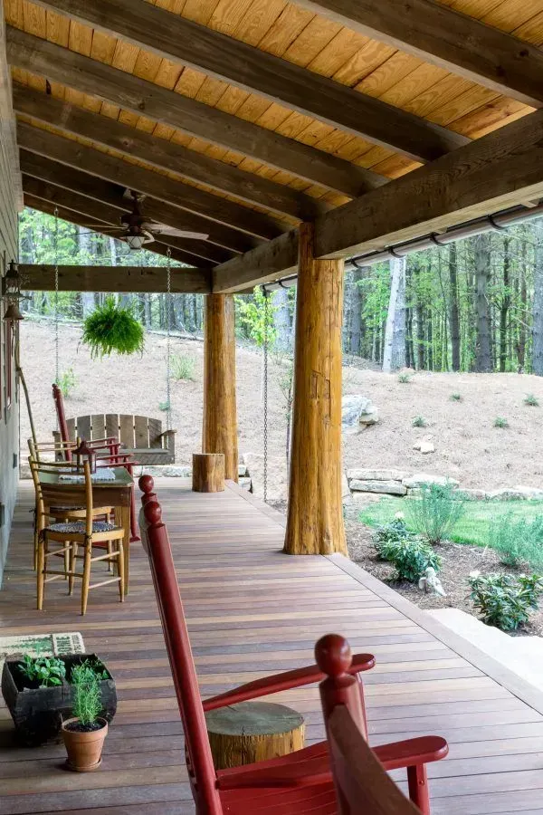 Wooden porch with red rocking chairs, rustic beams, and forest view.