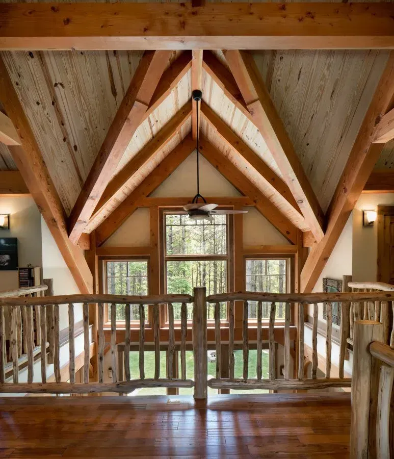 Wooden beam ceiling and railing. Windows overlooking trees. Interior view of a rustic lodge.