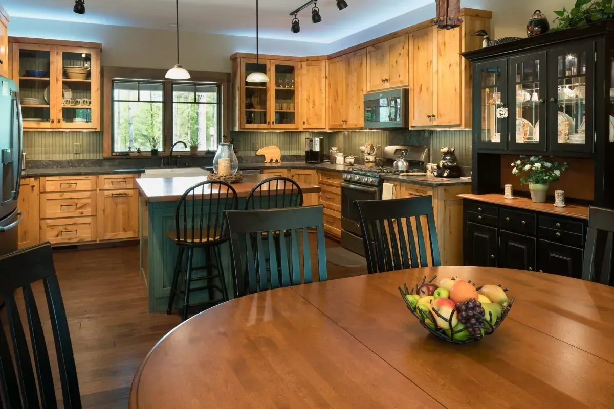 Rustic kitchen with wooden cabinets, island, table, and chairs; fruit bowl centerpiece.