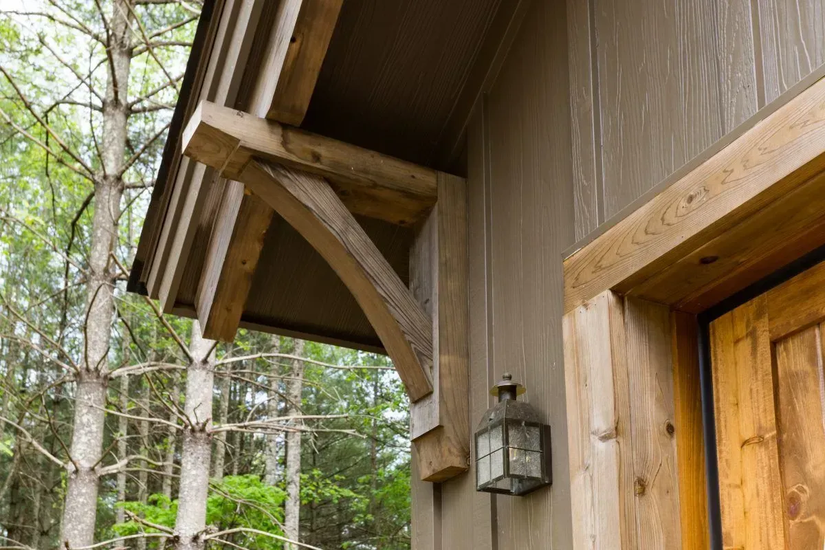Wooden porch detail with bracket, lantern, and door, surrounded by trees.