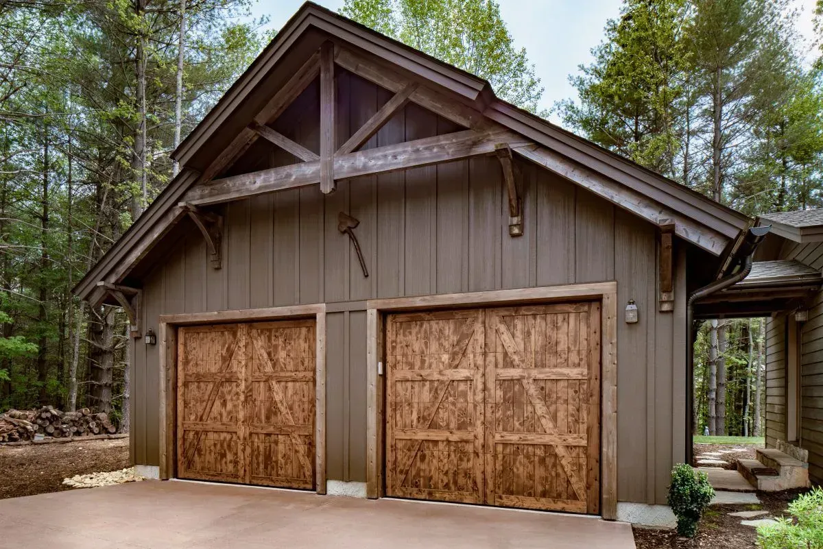 Brown garage with wooden doors and trim, nestled in a wooded area.