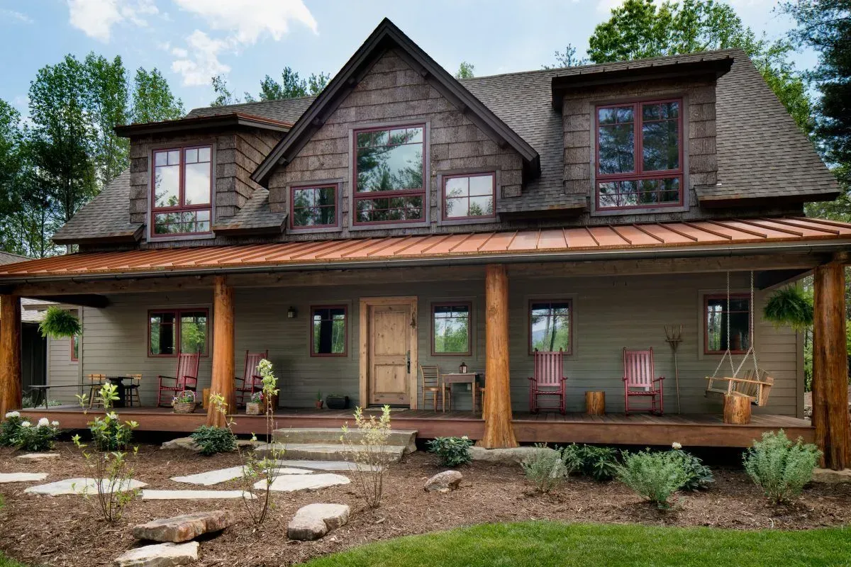 Rustic two-story home with a wraparound porch, wooden beams, and a stone pathway leading to the front door.