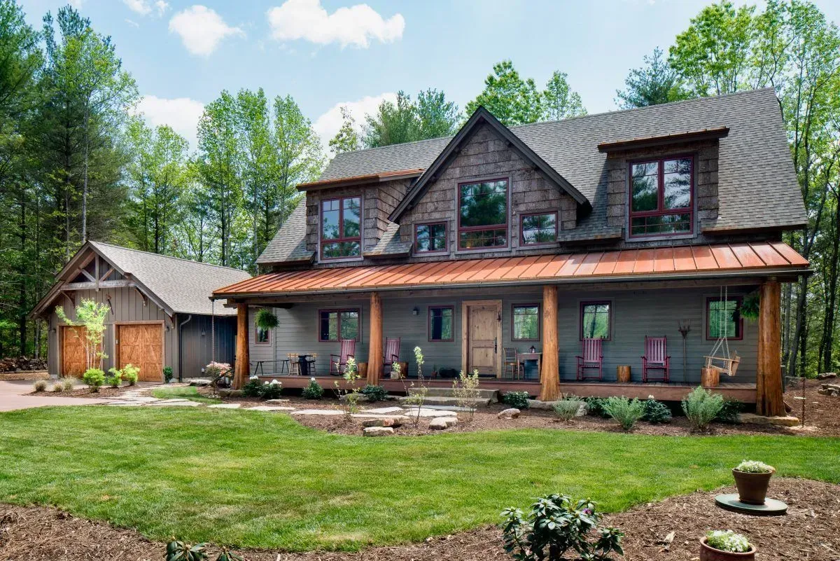 Two-story house with a porch and detached garage, surrounded by trees and a green lawn.