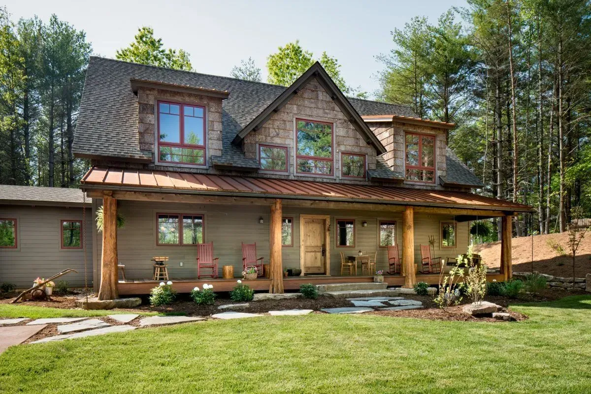 Rustic two-story house with stone and wood accents, front porch, and lush green lawn.