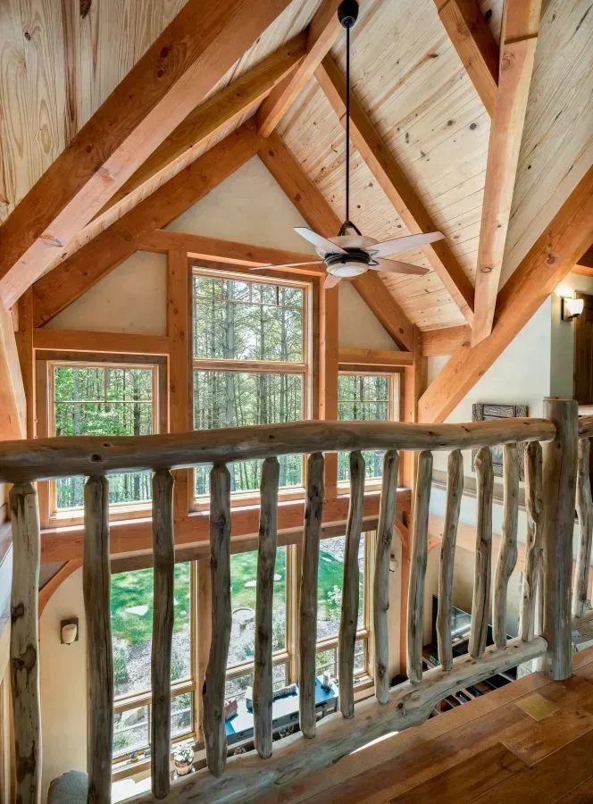 Wooden interior with log railing, windows overlooking trees, and exposed beams.
