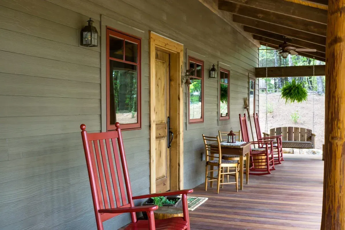 A porch with red rocking chairs, a wooden table, and a door, all under a wood roof.