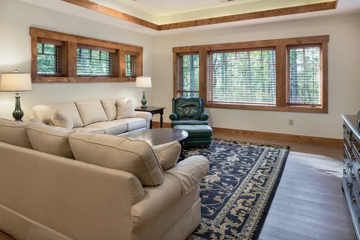 Living room with cream-colored sofas, wooden trim, area rug, and chair near windows.