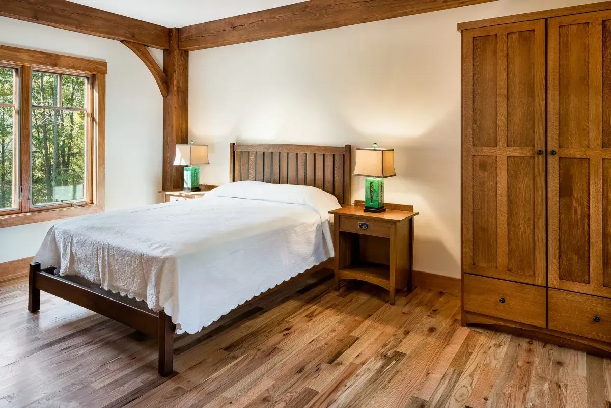Bedroom with wooden bed, nightstands, wardrobe, and hardwood floor; window with greenery view.