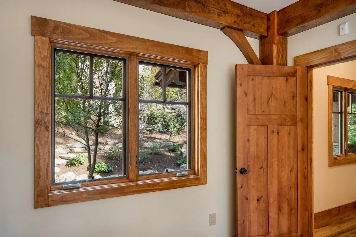 Wooden framed window and door in a room, offering a view of a lush outdoor area.