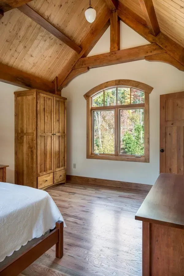 Wooden bedroom with an arched window, beams, and furniture.