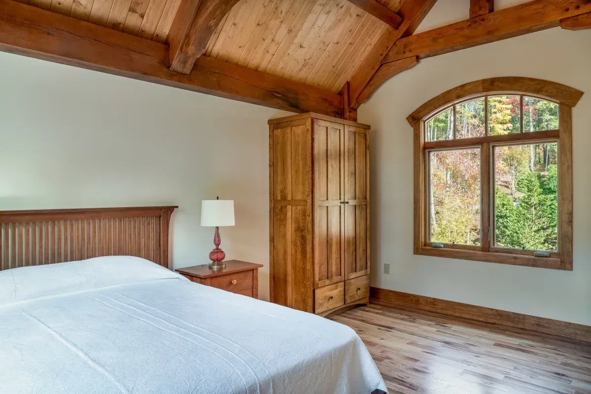 Bedroom with wooden bed, wardrobe, window, and exposed beams; sunlight.