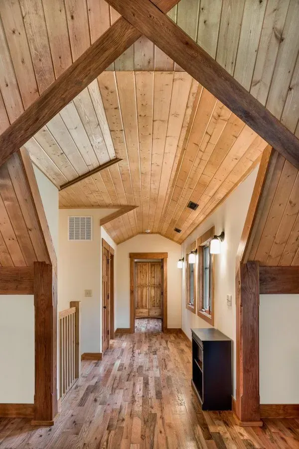 Wooden hallway with wood ceiling, trim, and floor. Light fixtures on wall.