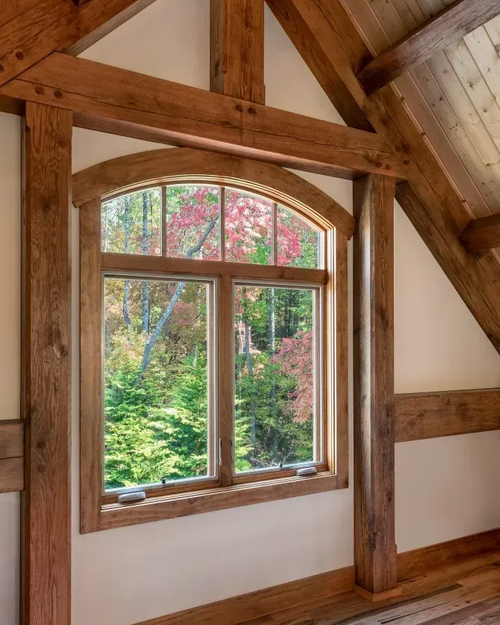 Window framed by wooden beams, overlooking a colorful forest, natural light illuminates the interior.