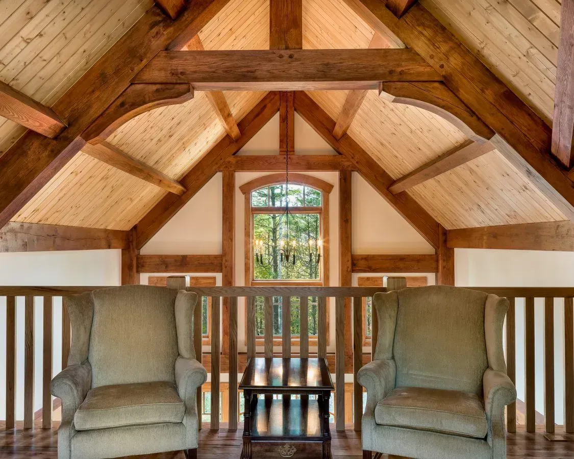 Two armchairs face a window in a room with wood beams and a railed balcony.
