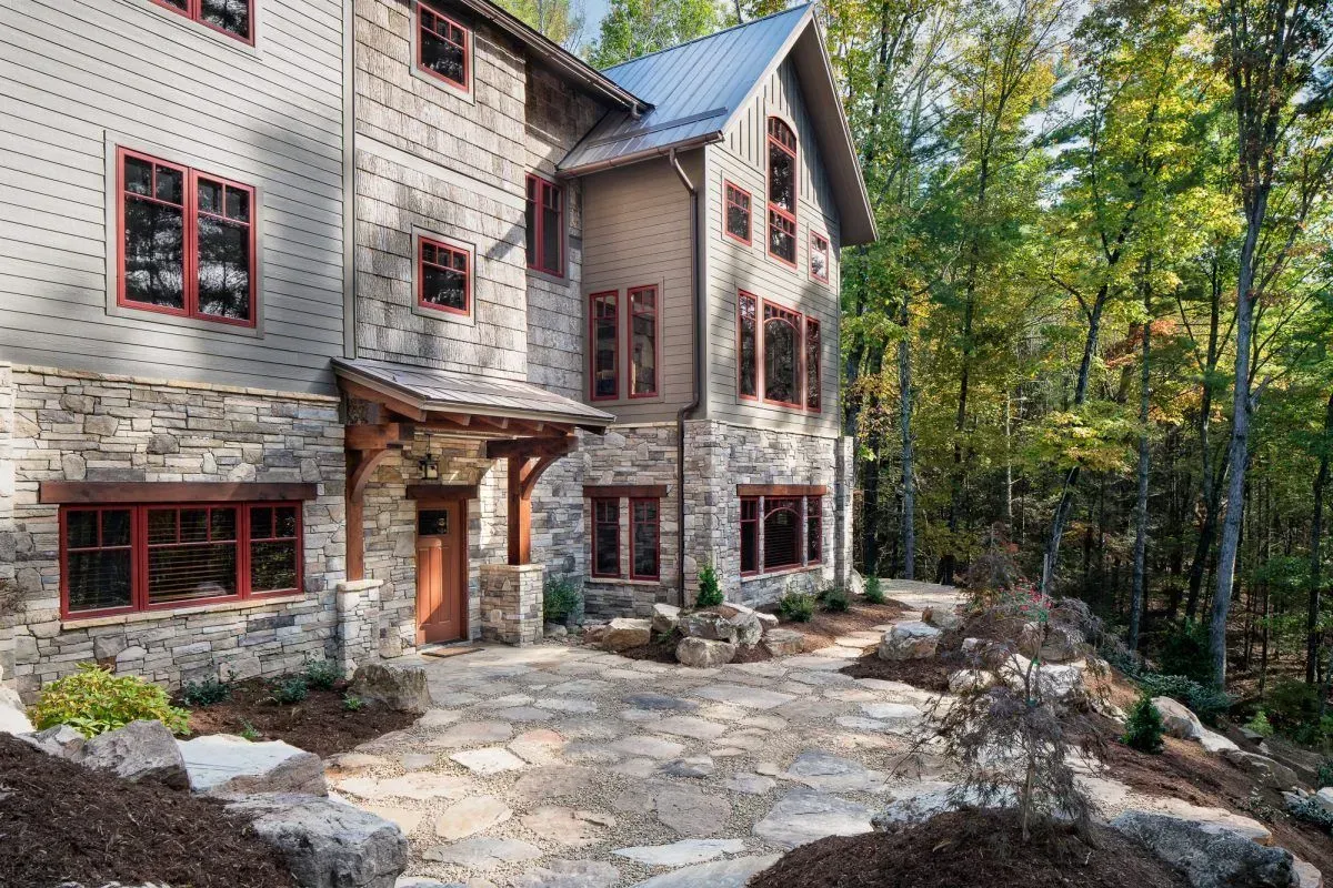 Stone and wood cabin with red window frames in a wooded setting.