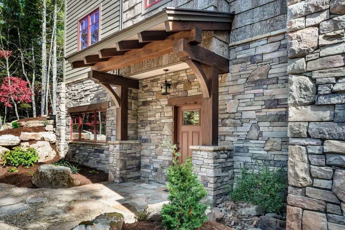 Stone-clad home with a wooden pergola over the front door.