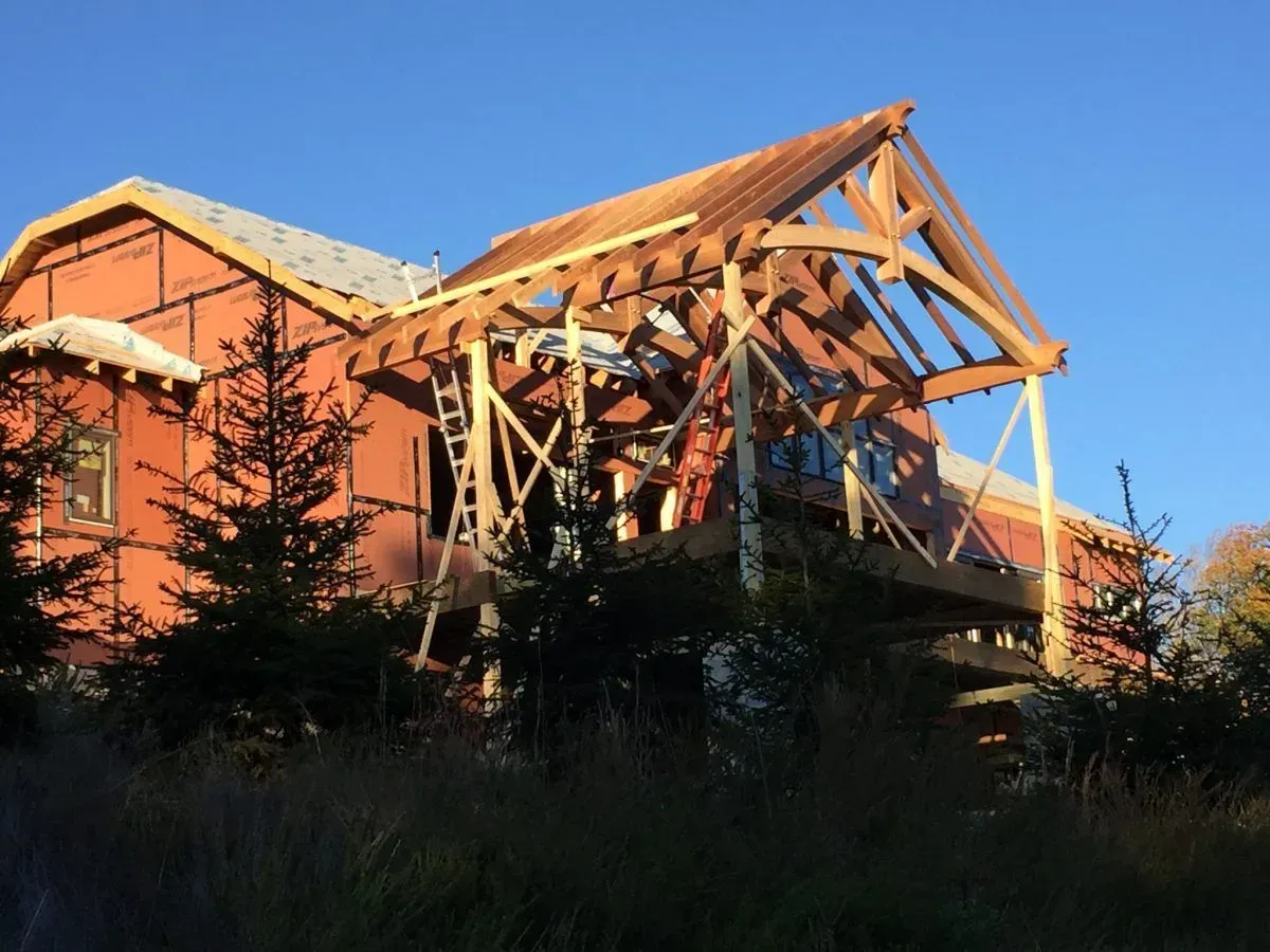 House under construction, red siding, wooden framework for porch, clear blue sky.