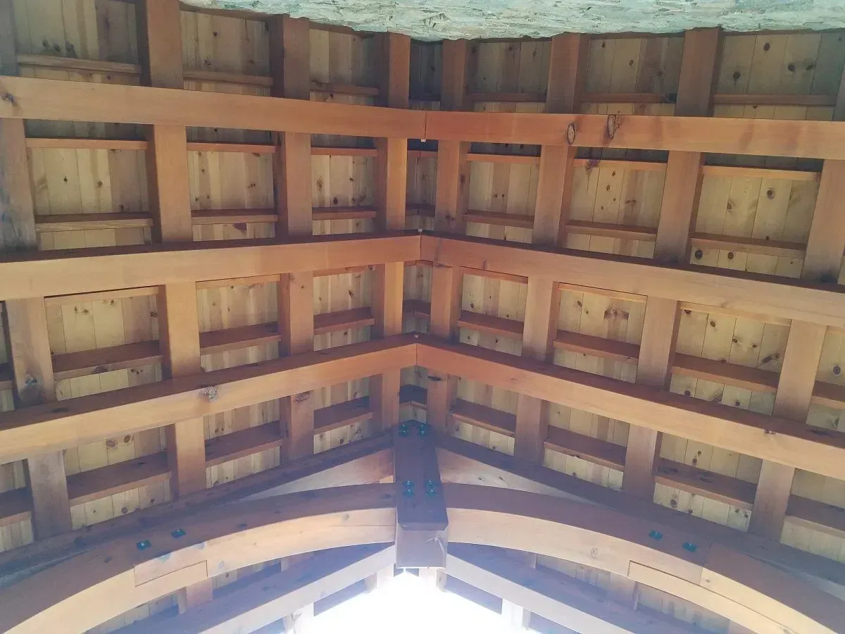 Wooden ceiling beams converge at a central point, revealing the underside of a structure. Brown beams and wood panels.