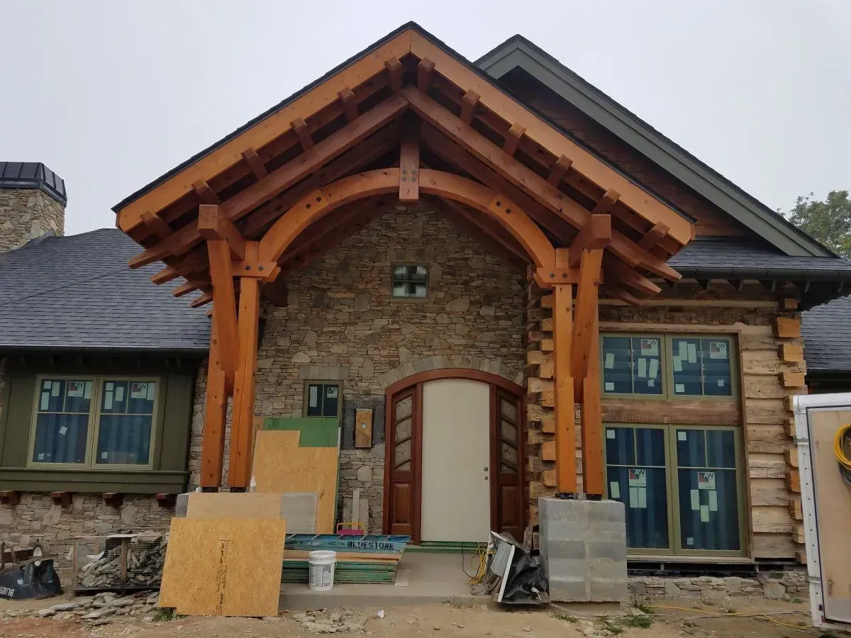 Rustic house entrance with wooden beams, stone walls, and arched doorway.