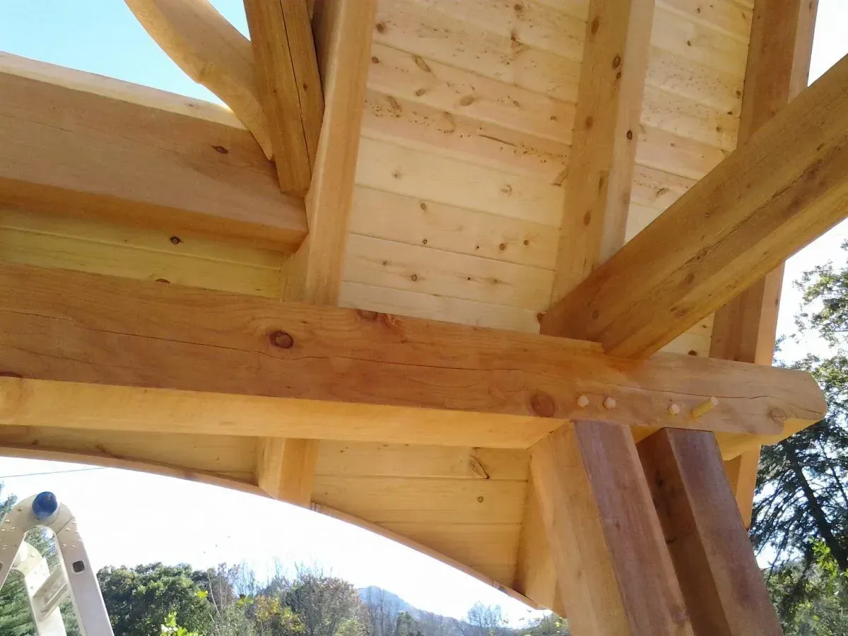 Wooden timber frame construction with beams, posts, and ceiling boards; natural wood tones.