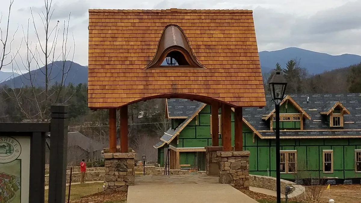 Arched wooden gateway with a unique copper-trimmed window, leading to houses against a mountain backdrop.