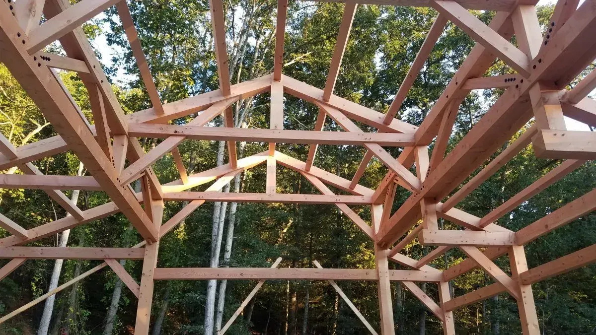 Wooden timber frame of a building in a forest, unfinished roof structure.