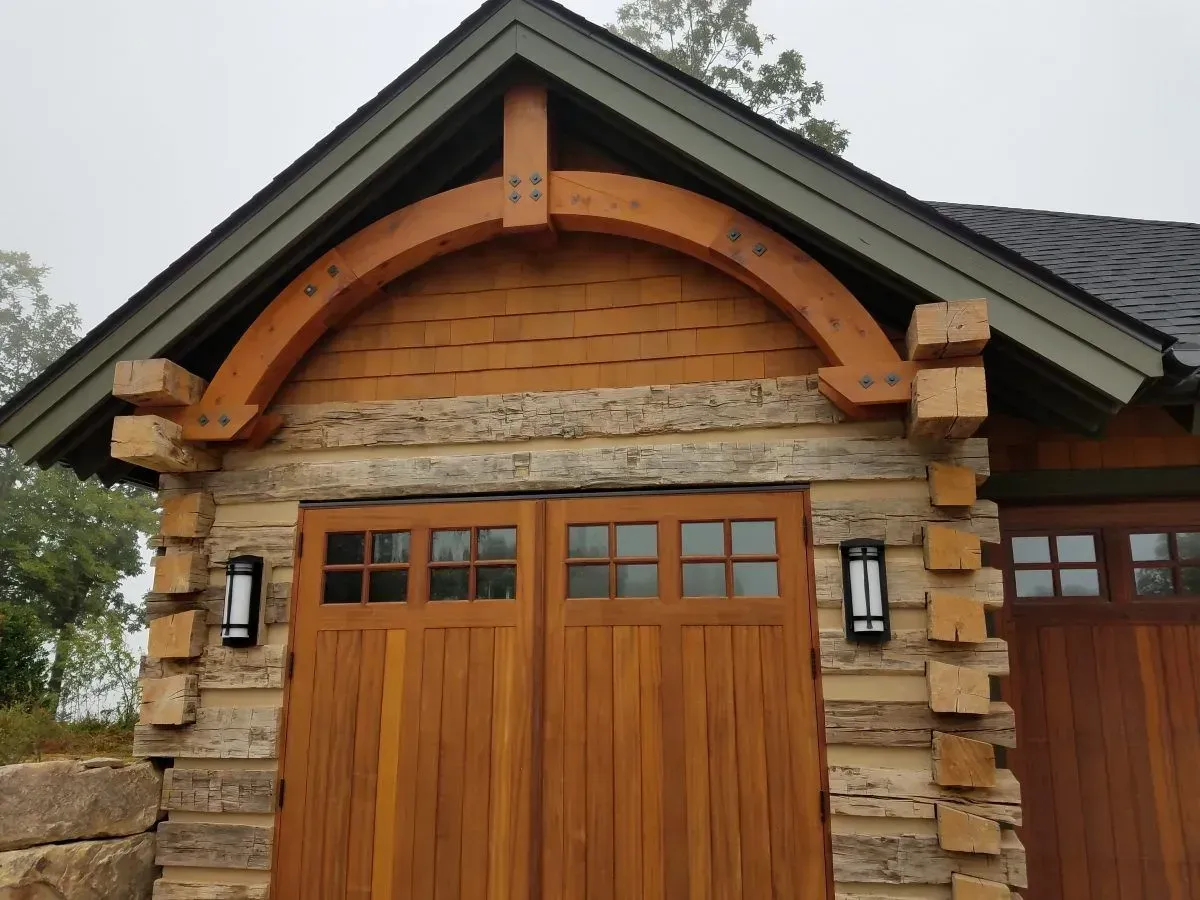 Wooden garage with arched beam over the doors, set in a log cabin style building.
