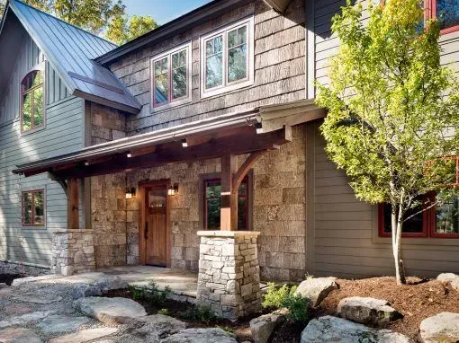 Rustic home exterior with stone and wood accents; entry with porch, and landscaping.