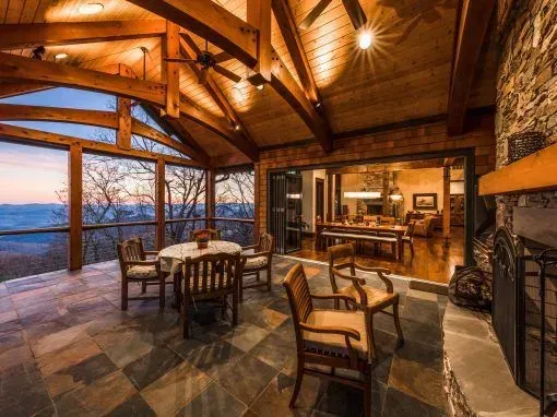 Open-air porch with stone floor, dining table, chairs, and fireplace; interior visible through sliding glass doors.
