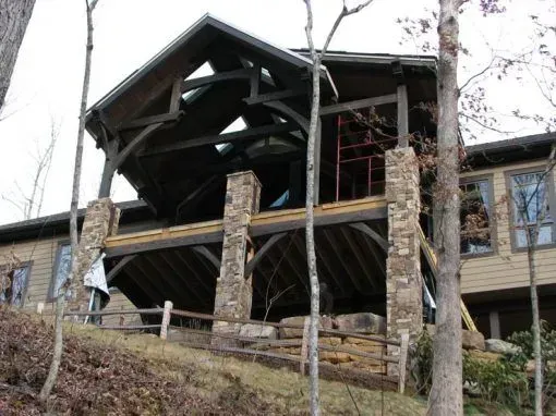 Cabin exterior with stone pillars, wood beams, and a partially built roof on a hillside.