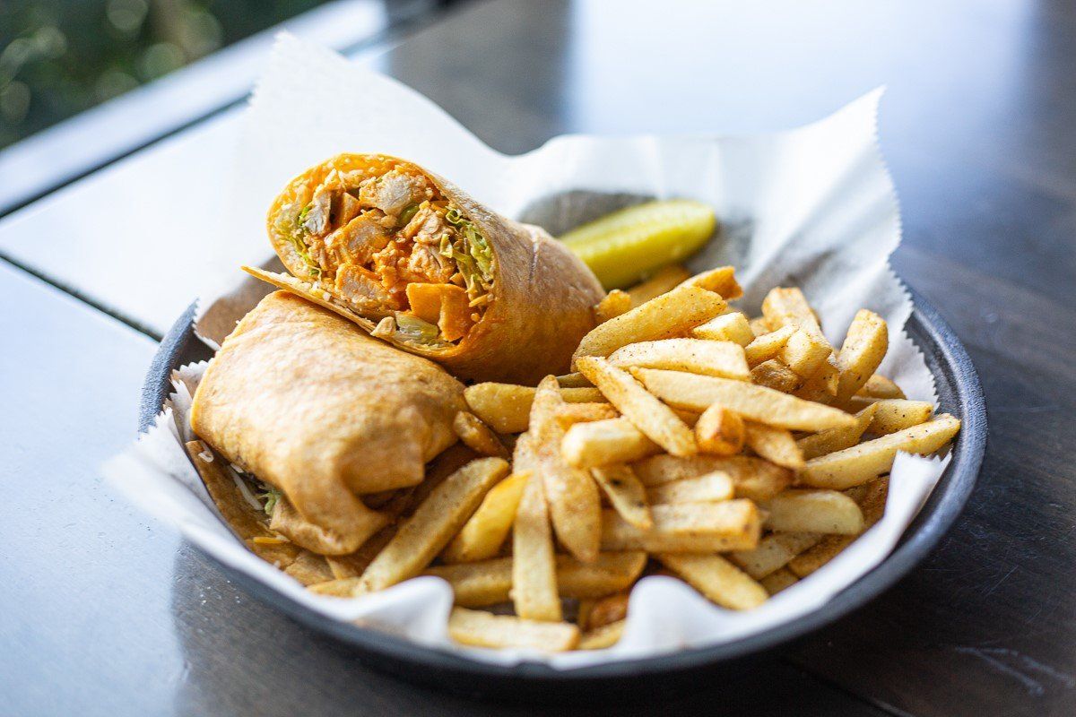 A wrap and french fries on a plate on a table.