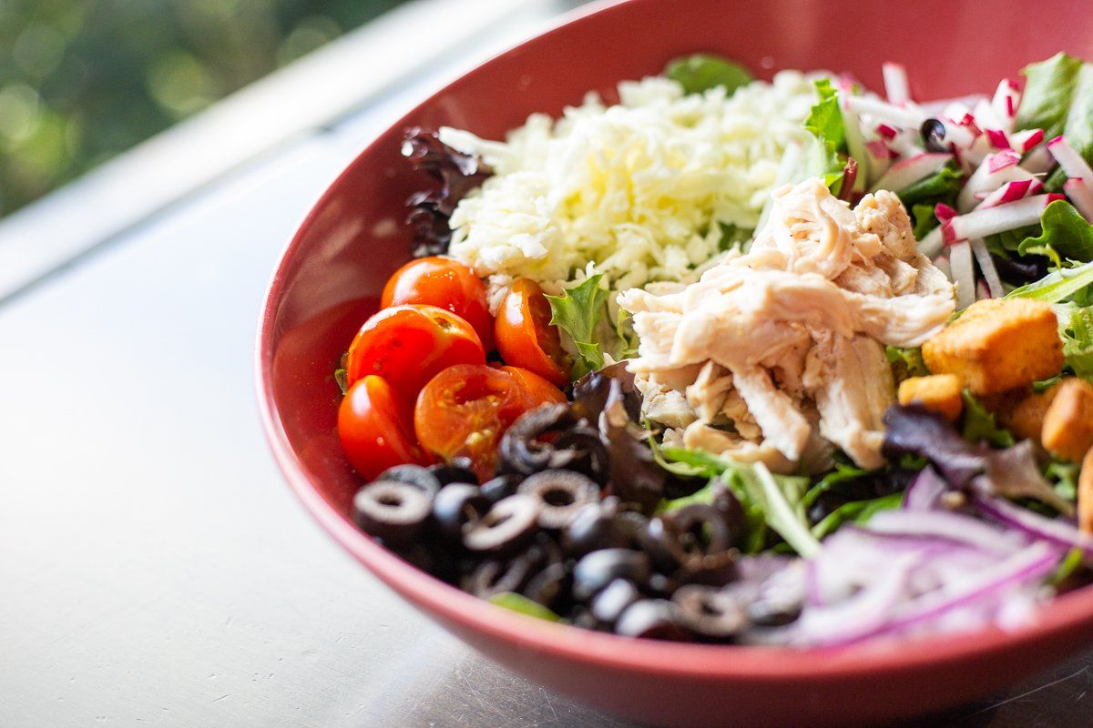 A close up of a salad in a red bowl on a table.