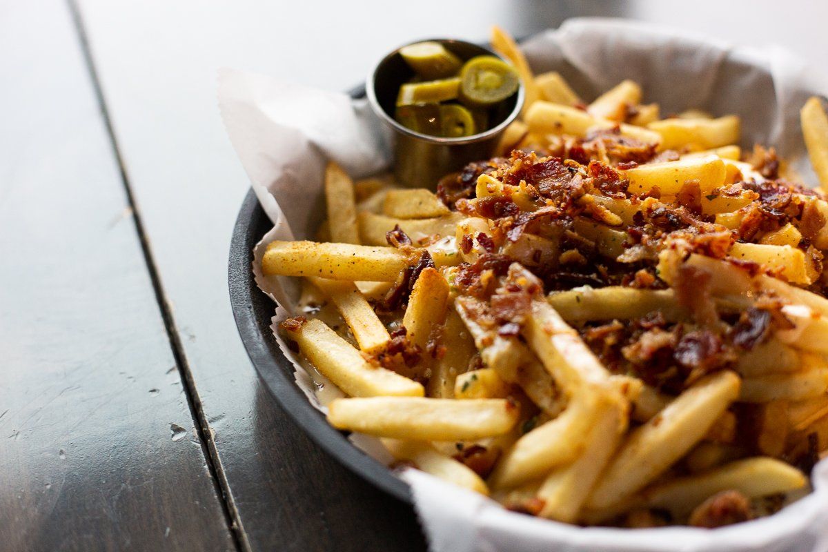 A basket of french fries with bacon and jalapenos on a table.