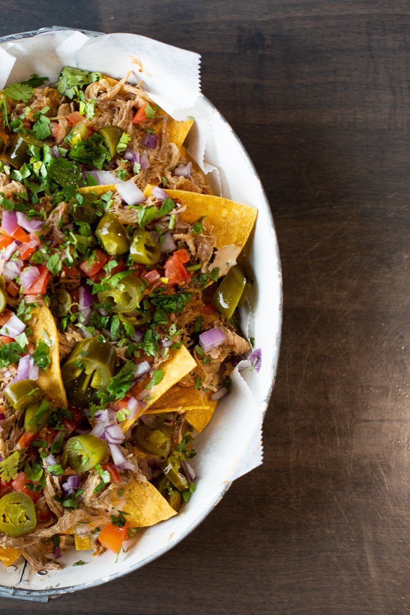 A bowl of nachos with meat and vegetables on a wooden table.