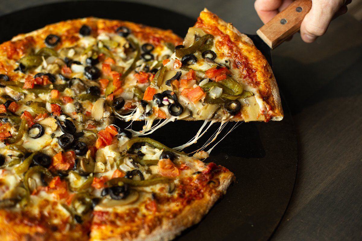 A person is taking a slice of pizza with a spatula.
