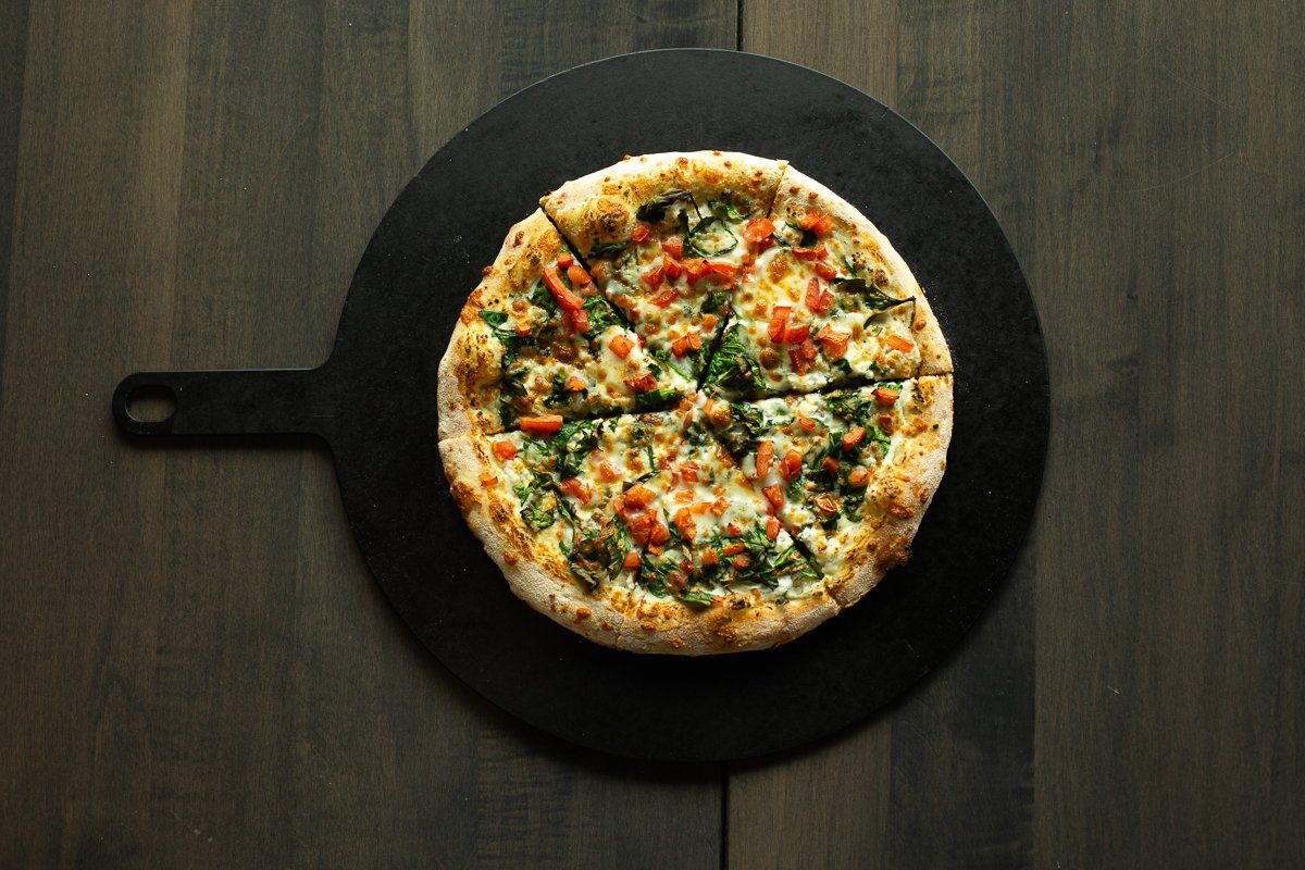 A pizza is sitting on a black cutting board on a wooden table.