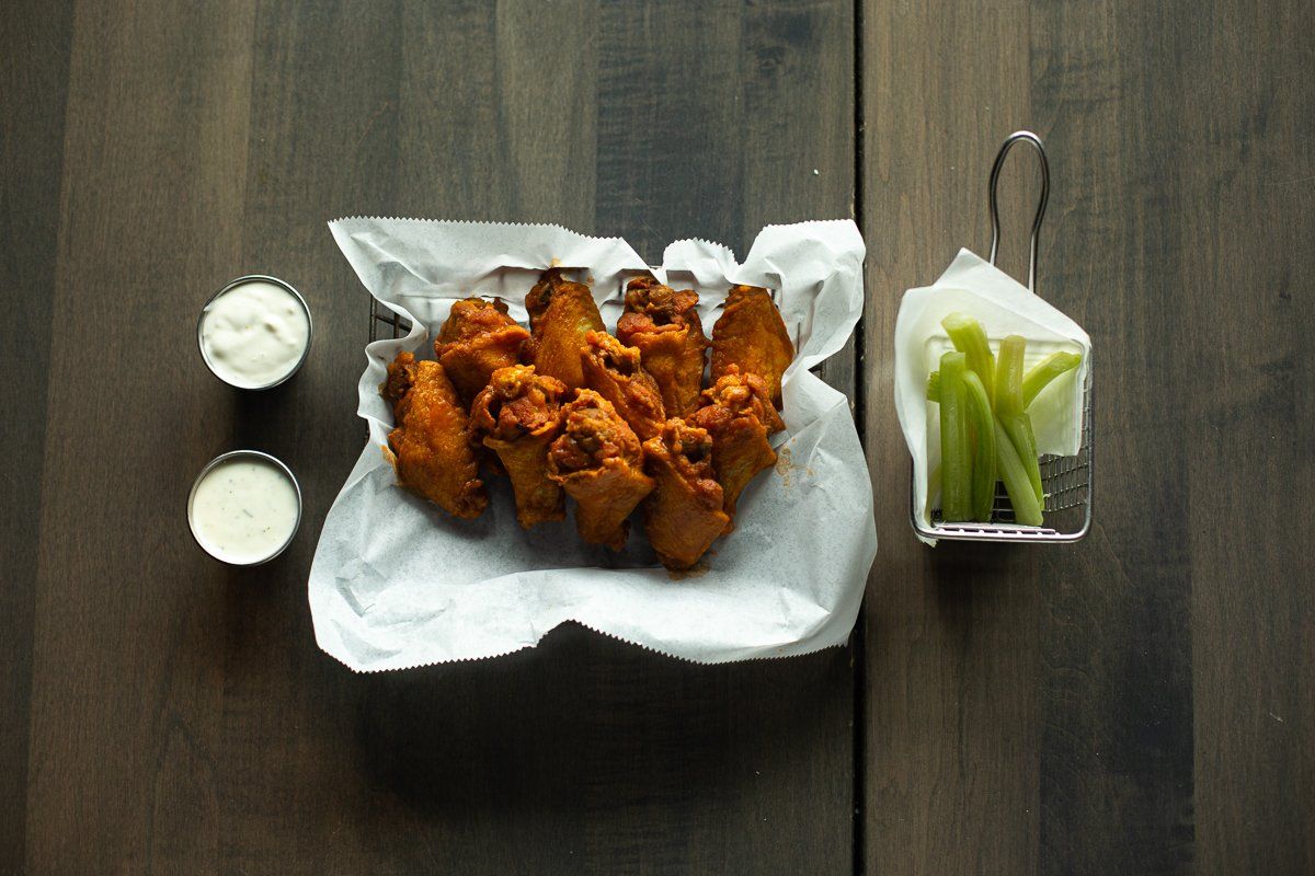 A basket of chicken wings and celery sticks on a wooden table.