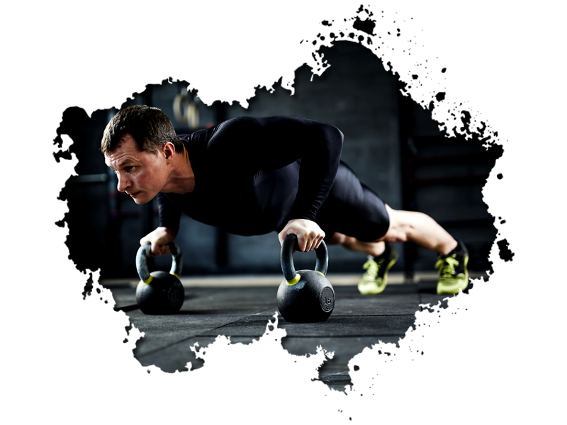 Man doing push-ups on kettlebells in a gym; wearing black athletic clothing.