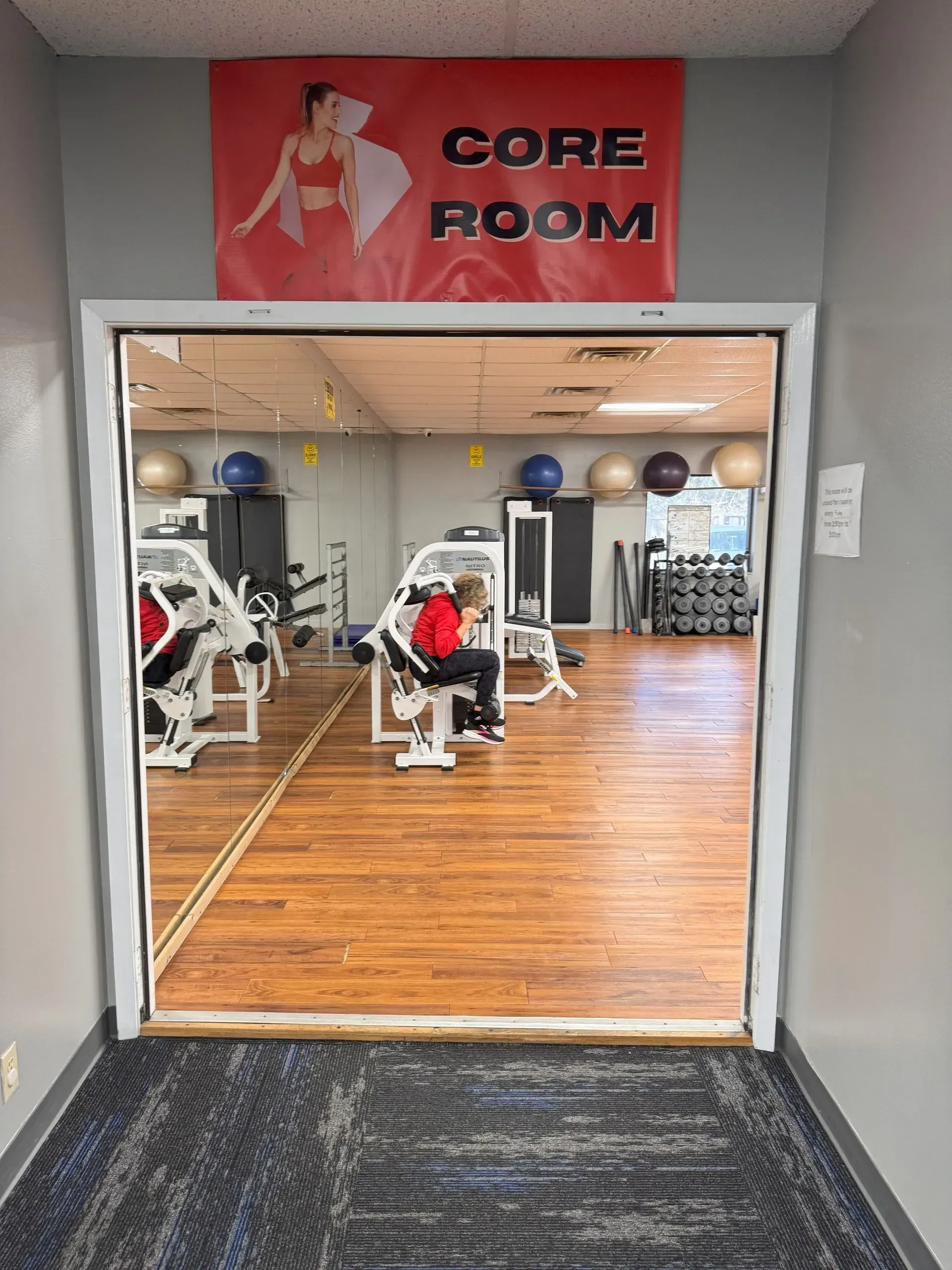 Entrance to a fitness room.  Sign reads "CORE ROOM".  Inside are workout machines, a person using one, and exercise balls.