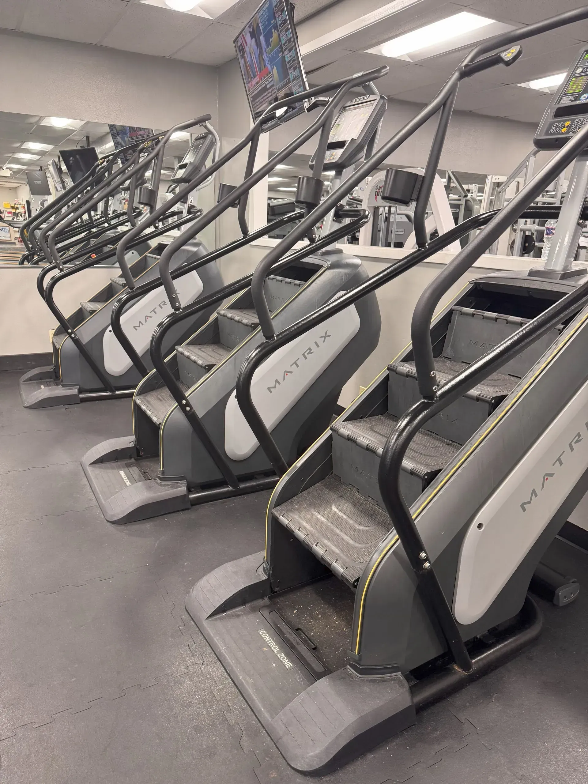 A row of Matrix stair steppers in a gym, with handles and display screens.