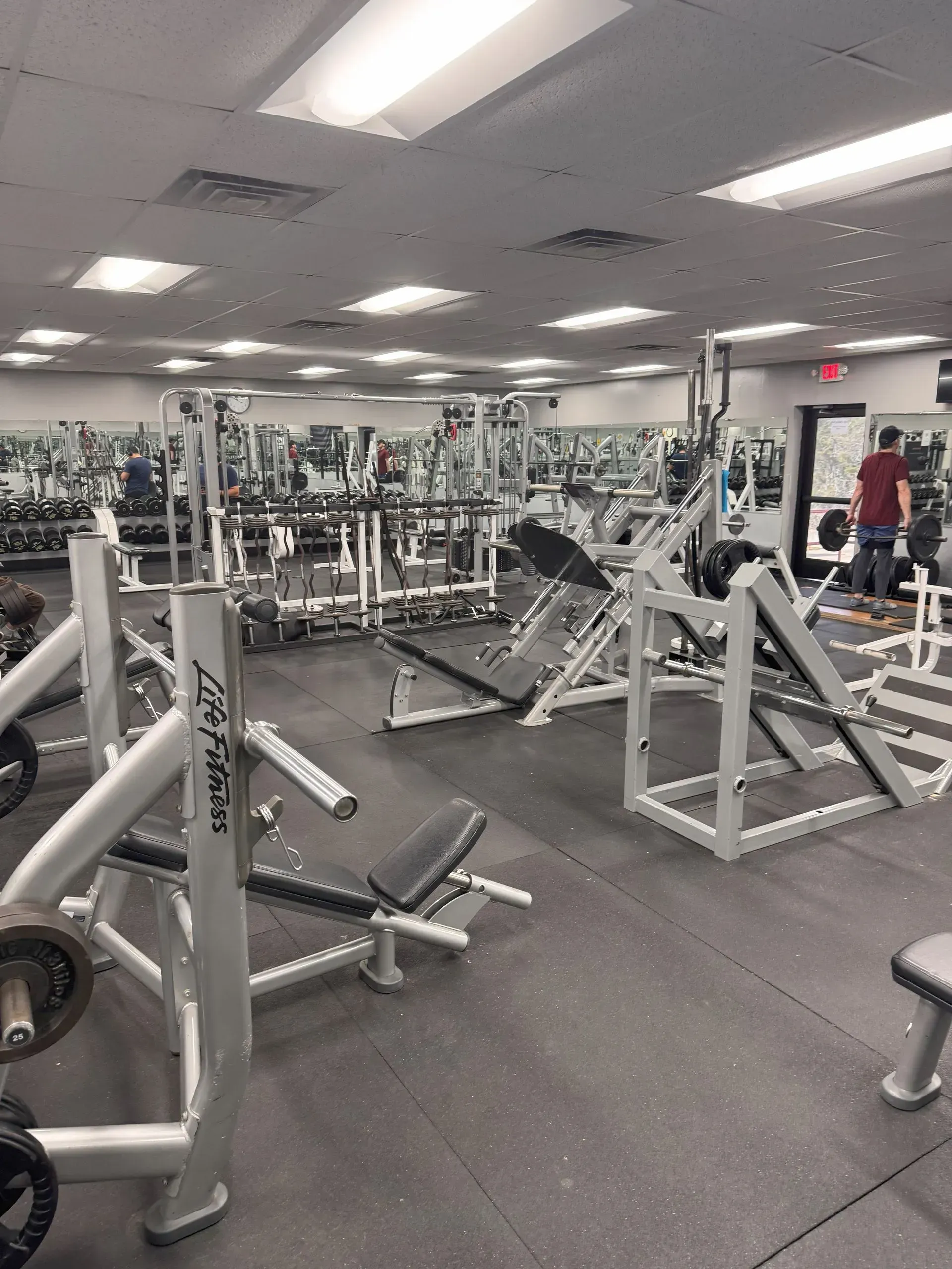 Gym interior with weight machines, a person, and many mirrors.