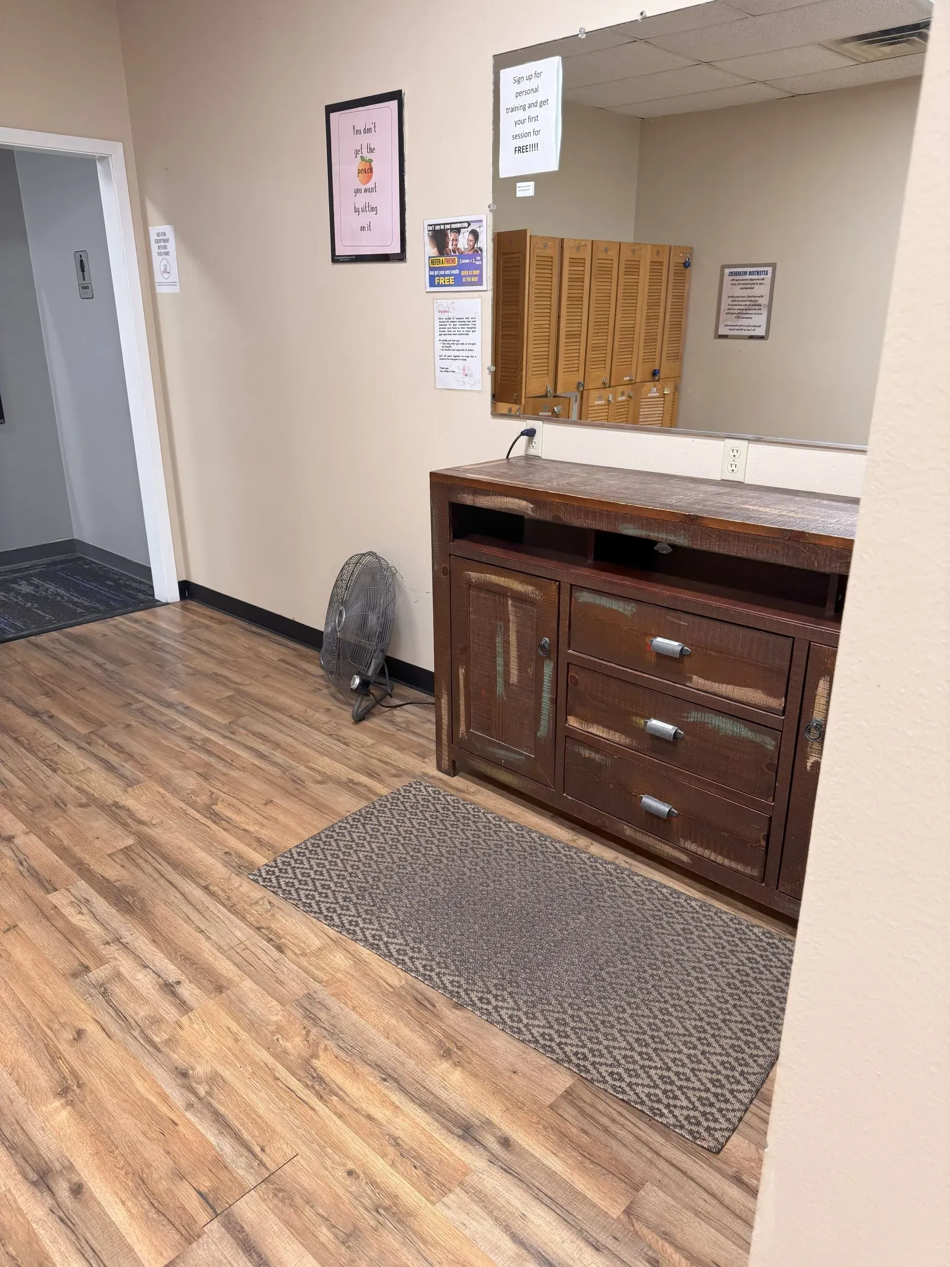 Hallway with wood-look floor, brown cabinet, rug, mirror. Includes fan and doorway to a carpeted room.