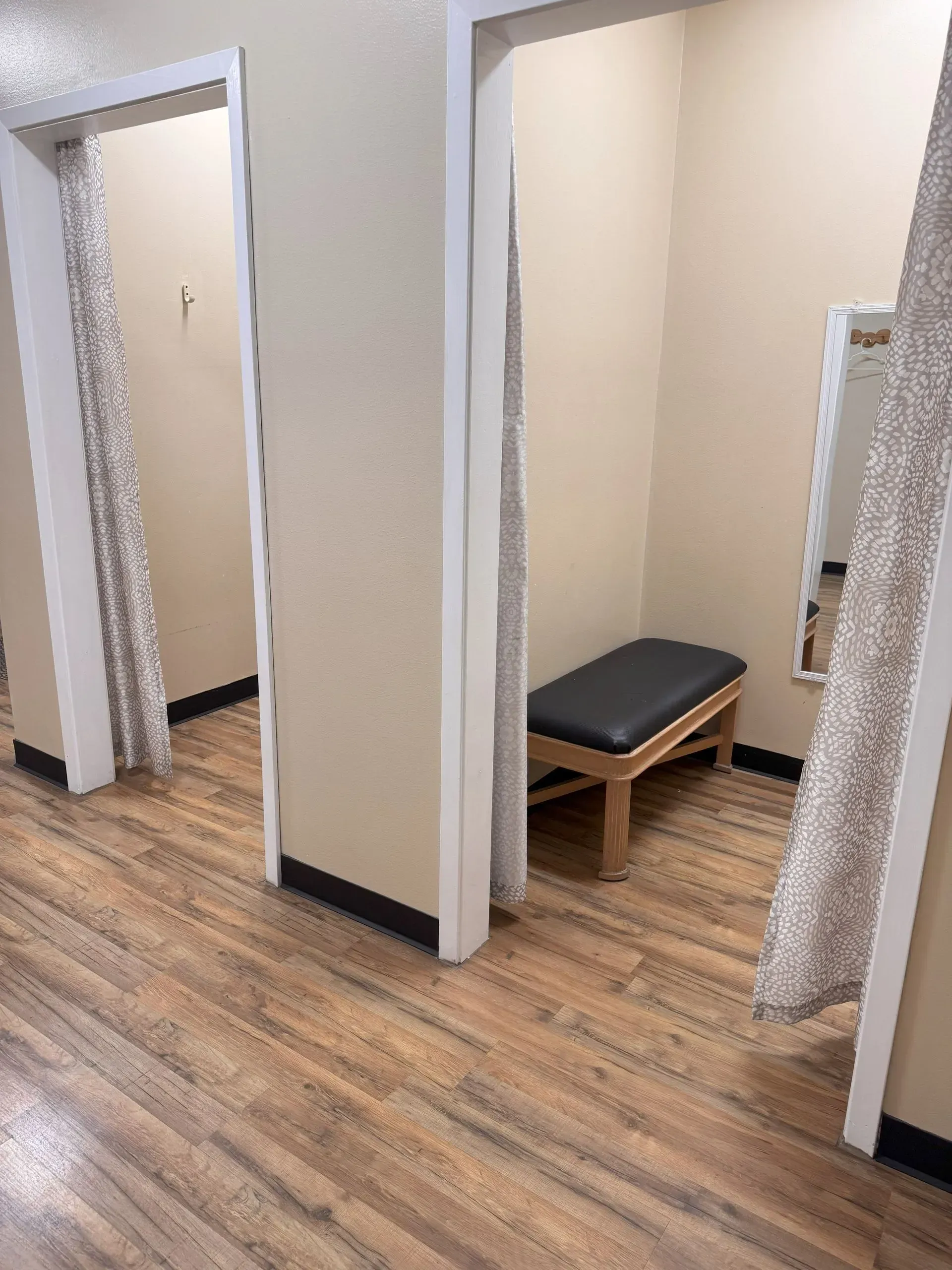 Three clothing store dressing rooms with tan walls, light wood floors, and benches.